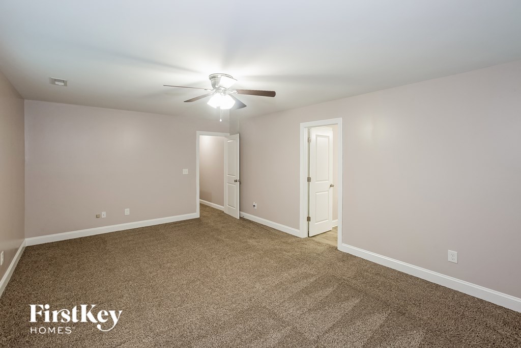 A carpeted room with a ceiling fan and two doors.