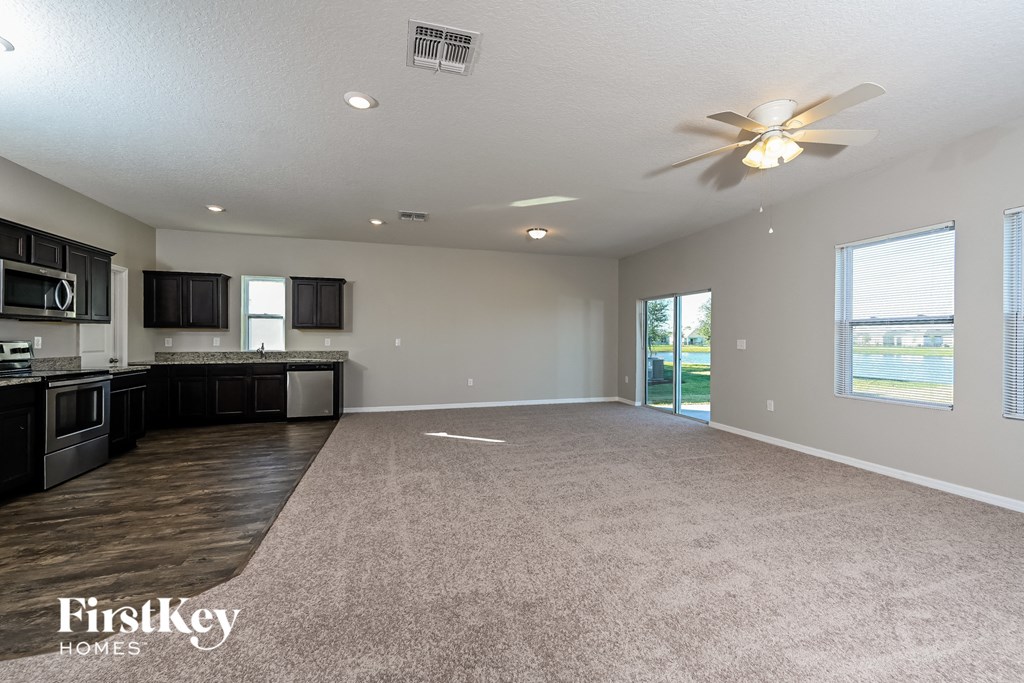 an empty living room with a kitchen and a ceiling fan