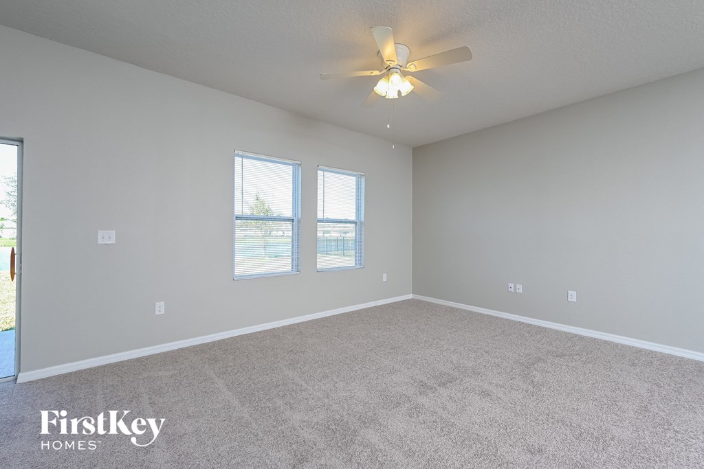 the spacious living room with ceiling fan and two windows