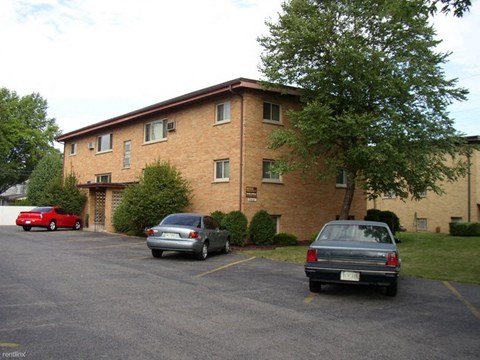 A parking lot with a red car and a grey car parked in front of a brick building.