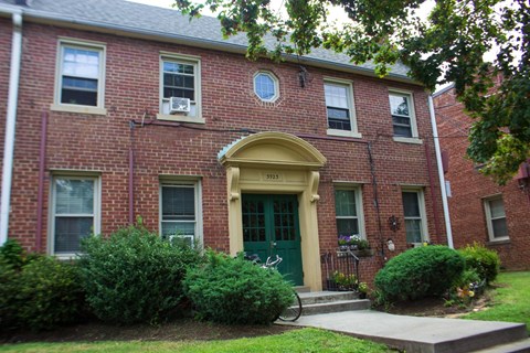 A red brick building with a green door and a yellow arch above it.