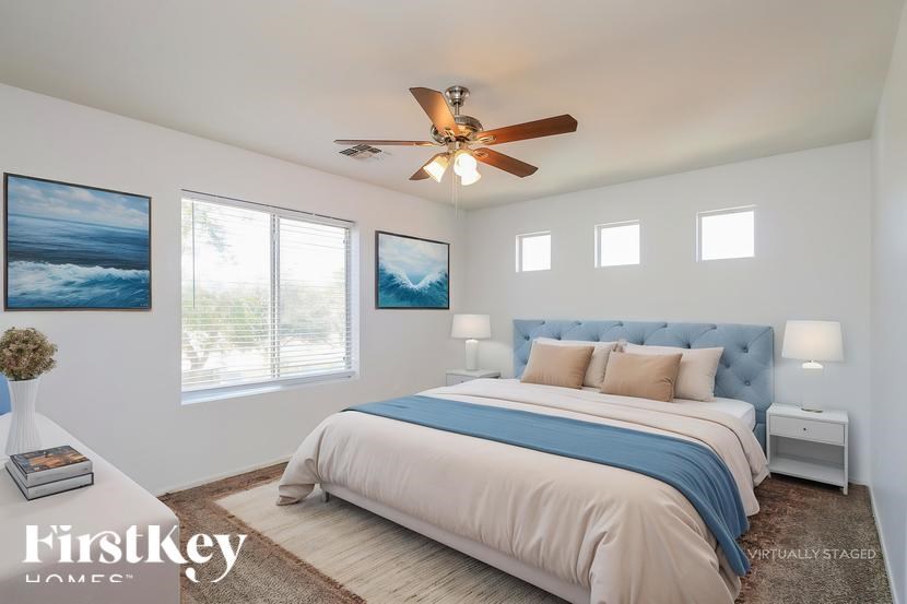 A bedroom with a bed, a ceiling fan, and a painting on the wall.