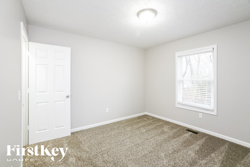 A room with a carpeted floor, a door, and a window with blinds.