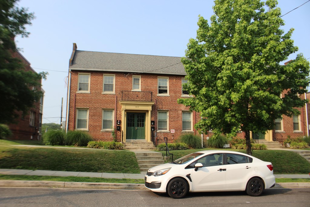 A white car is parked in front of a red brick house.