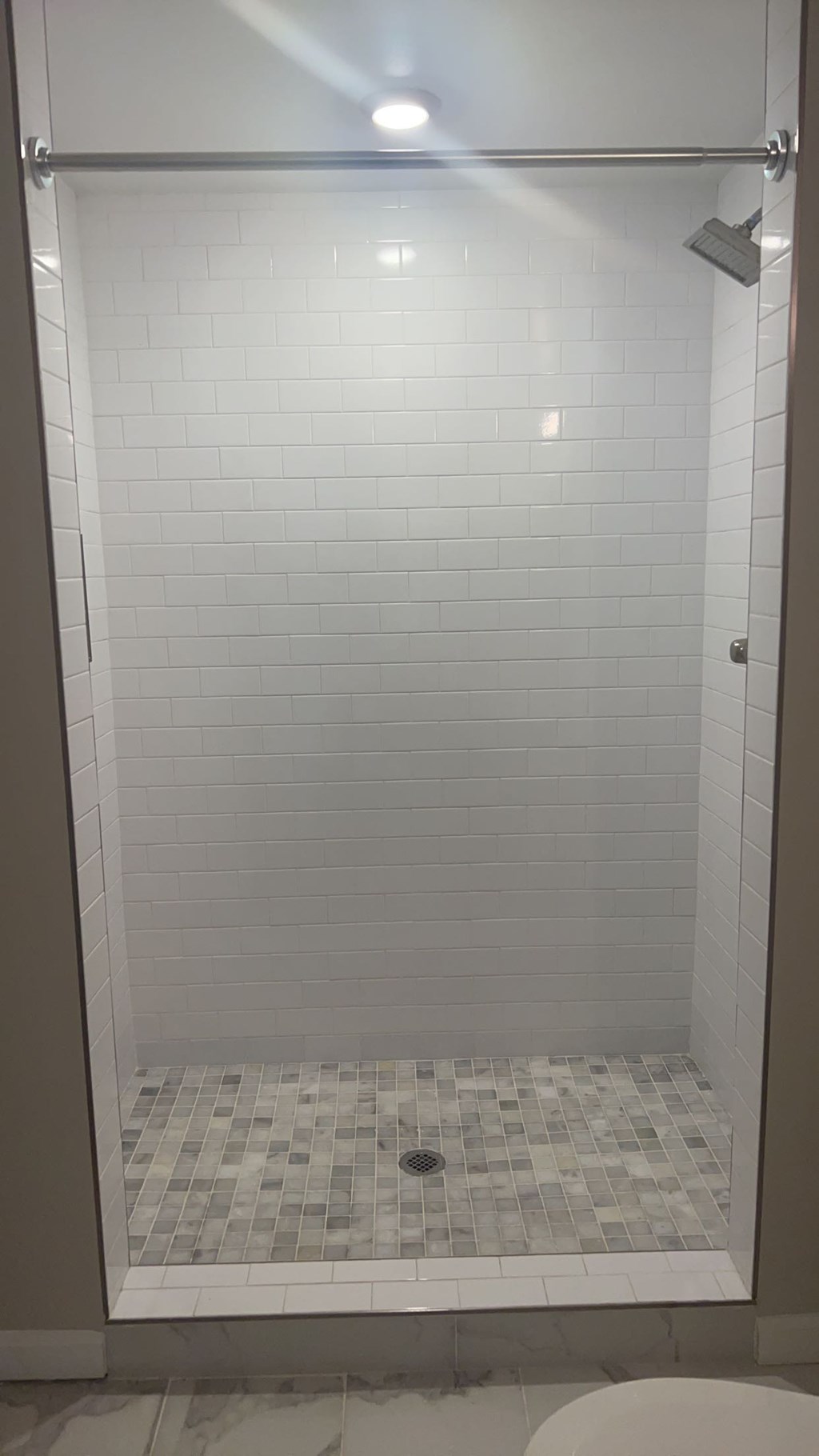 A white tiled shower with a drain in the middle.