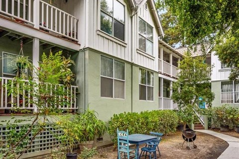 A green building with a balcony and a table and chairs in front.