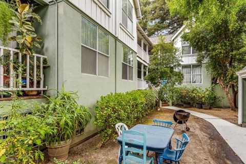 A patio with a table and chairs is surrounded by green plants.