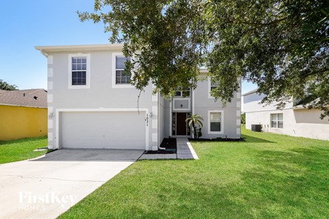 A white house with a garage is surrounded by a green lawn.