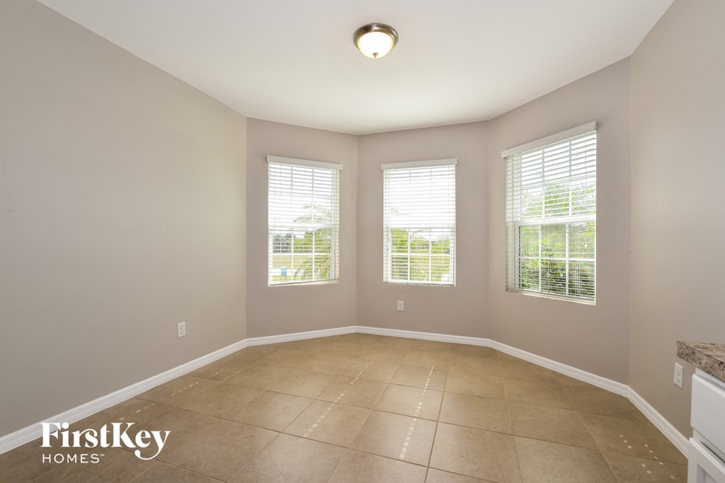 an empty dining room with three windows and a tiled floor