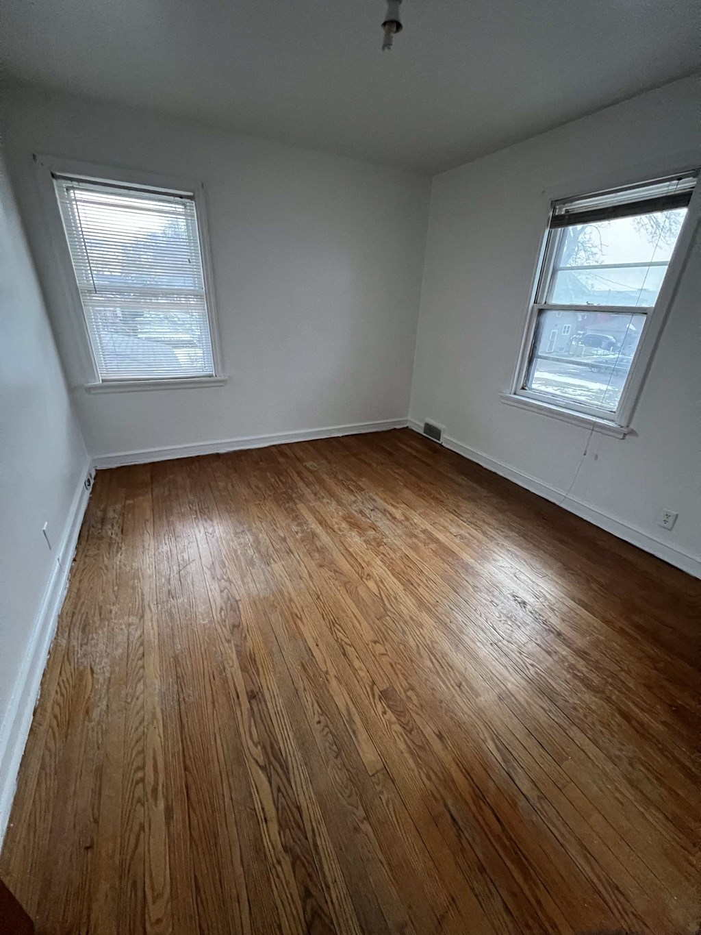 an empty room with wooden floors and two windows