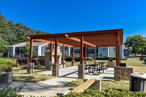 A wooden pavilion with a picnic table in front of apartment buildings.