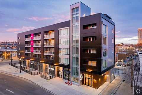 A modern multi-story building with a glass facade and a pink banner on the left side.