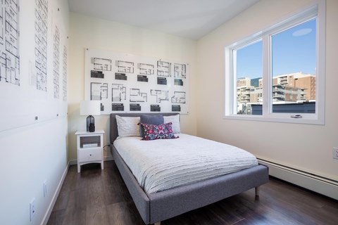 A bedroom with a bed, nightstand, and a wall of pictures.