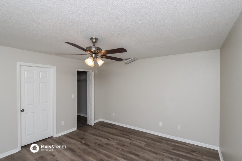 the spacious living room with ceiling fan and door to bedroom