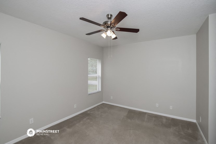 the spacious living room with ceiling fan and carpeting