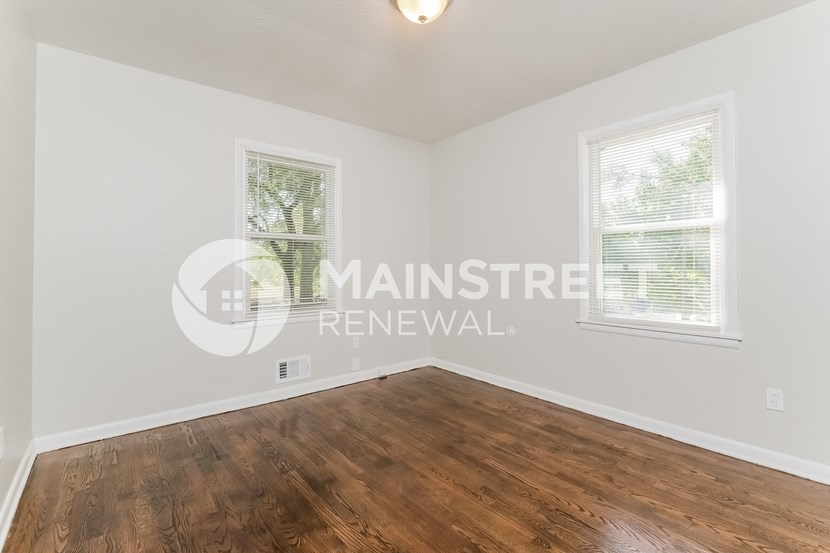 a bedroom with a hard wood floor and two windows