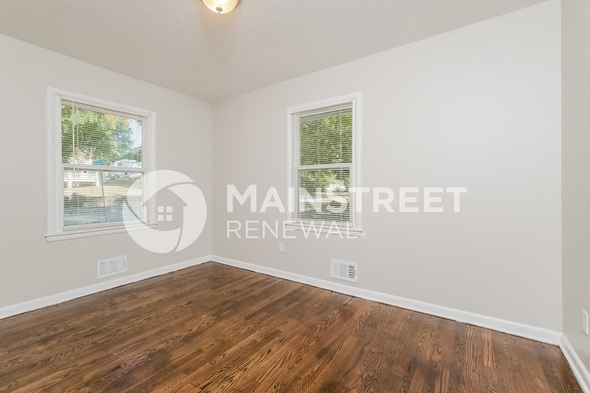 a bedroom with a hard wood floor and two windows