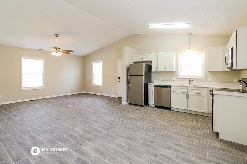 an empty living room with a kitchen and a ceiling fan