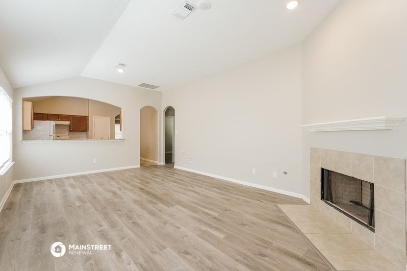 an empty living room with a fireplace and a kitchen