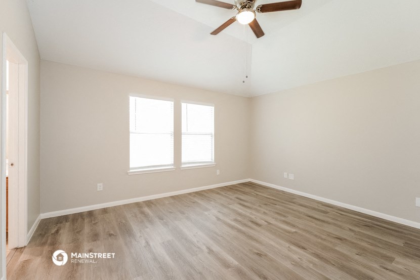 the spacious living room with wood flooring and a ceiling fan