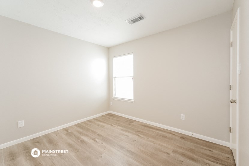 a bedroom with white walls and wood flooring and a window