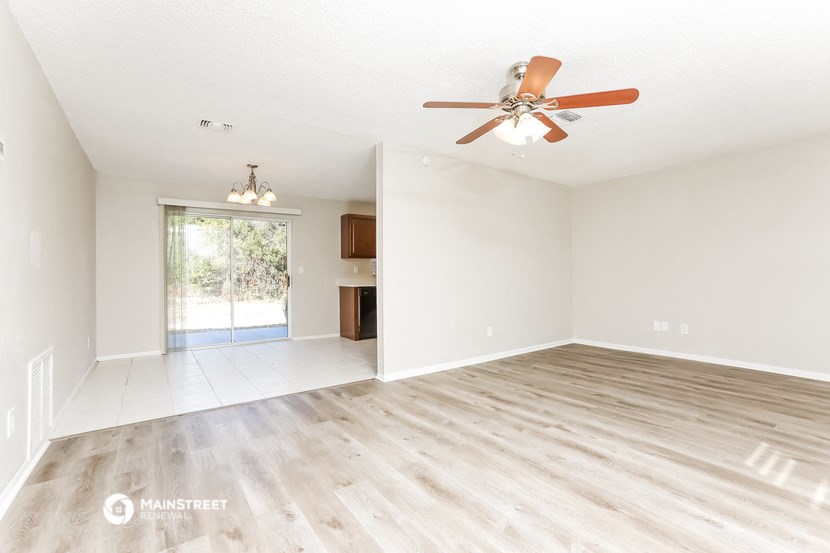the spacious living room with wood flooring and a ceiling fan