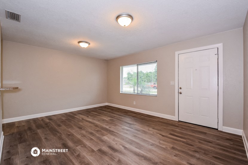the spacious living room with a white door and wood flooring