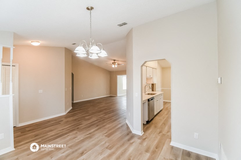 a spacious living room and kitchen with hardwood flooring and white walls