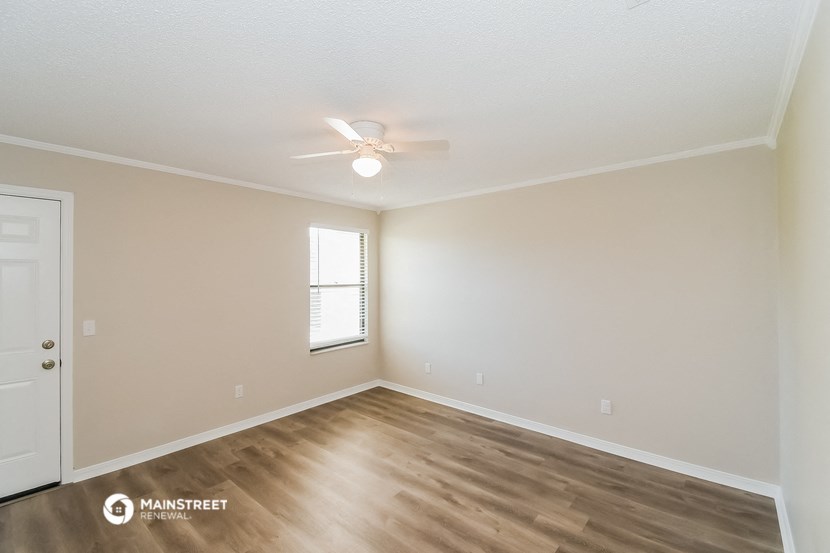 the spacious living room with hardwood flooring and a ceiling fan