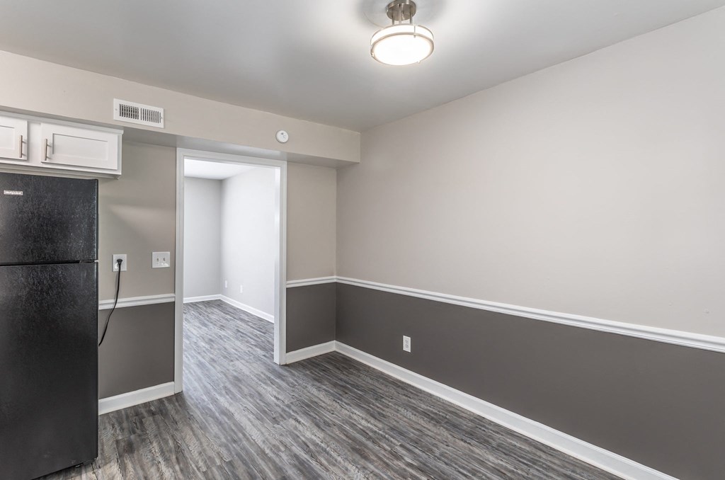 an empty living room with a refrigerator and a door to a kitchen