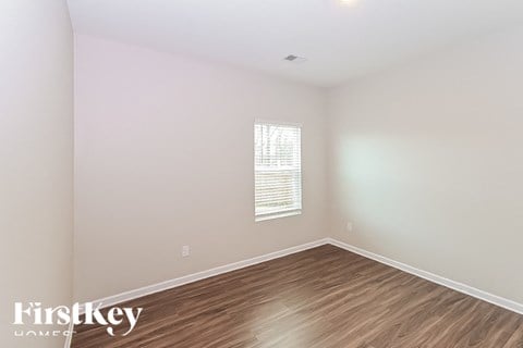 a bedroom with white walls and wood floors and a window