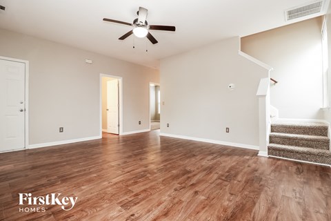 A spacious room with wooden floors and a staircase on the right side.