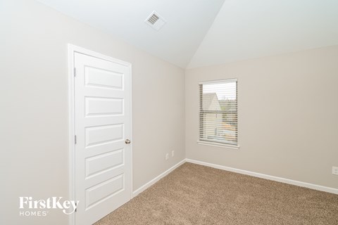 a bedroom with carpet and a white door and a window