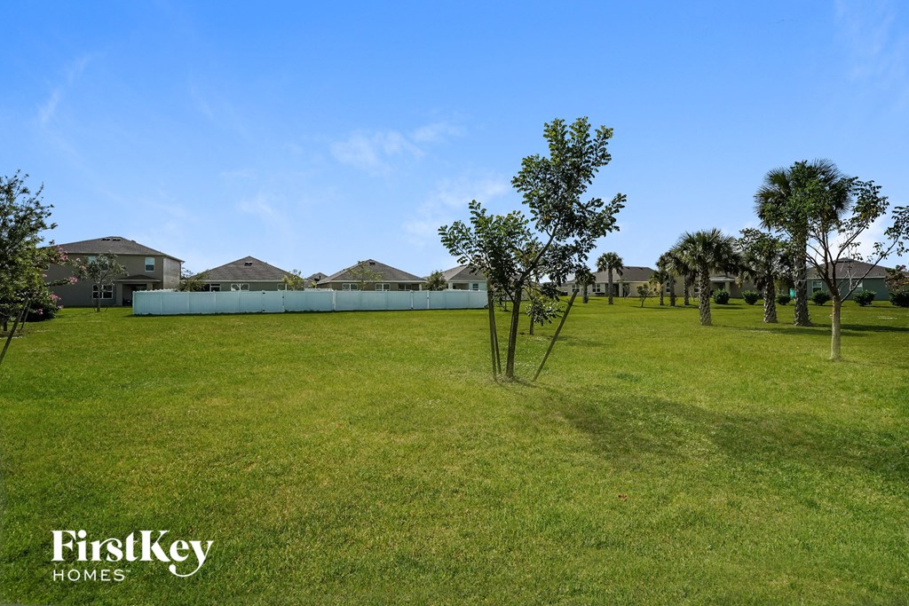 a large grass field with trees in front of a house
