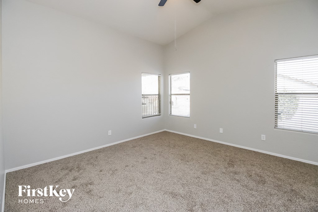 A spacious room with a carpeted floor and two windows.