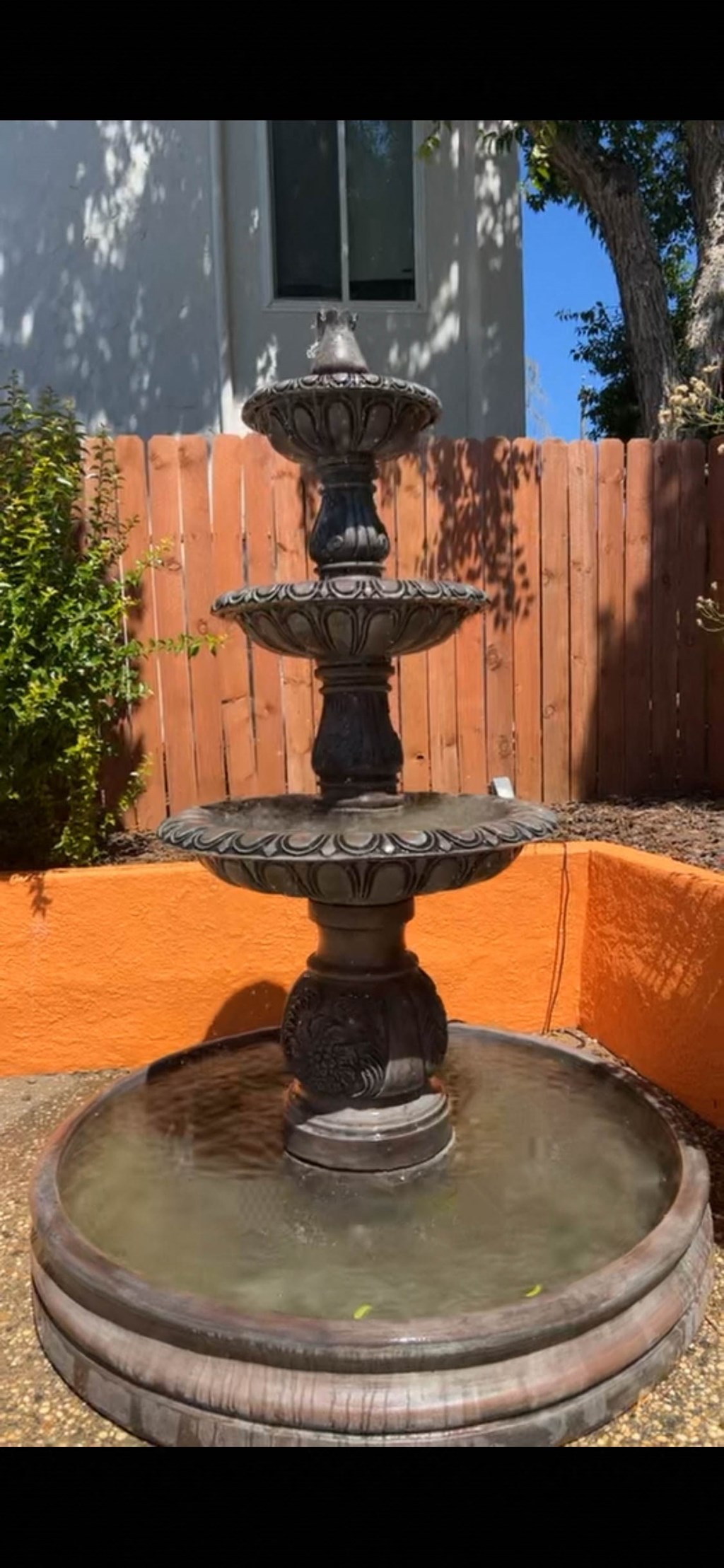 a water fountain in a backyard in front of a fence
