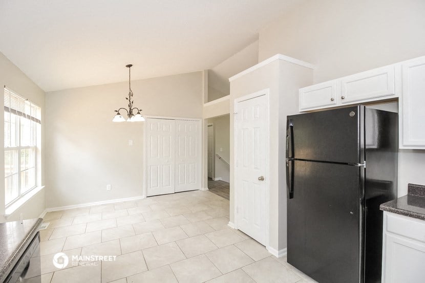an empty kitchen with a black refrigerator and white cabinets