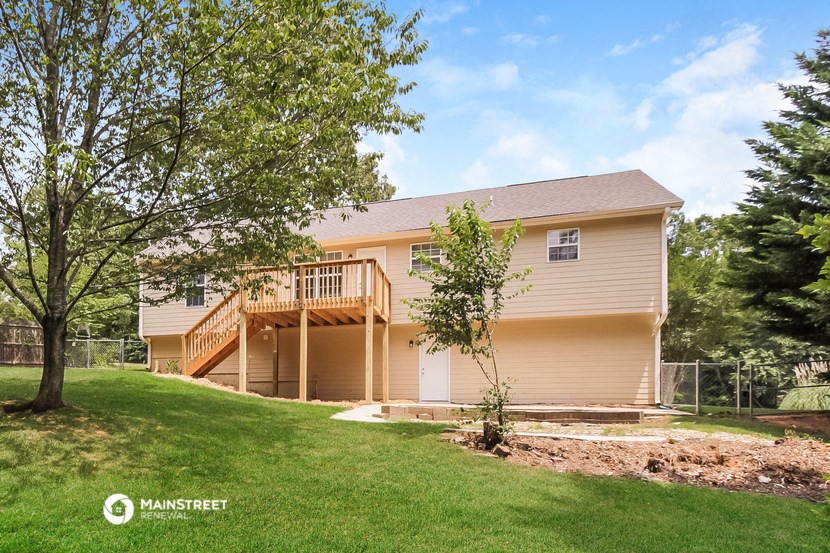 the front of a yellow house with a yard and a deck