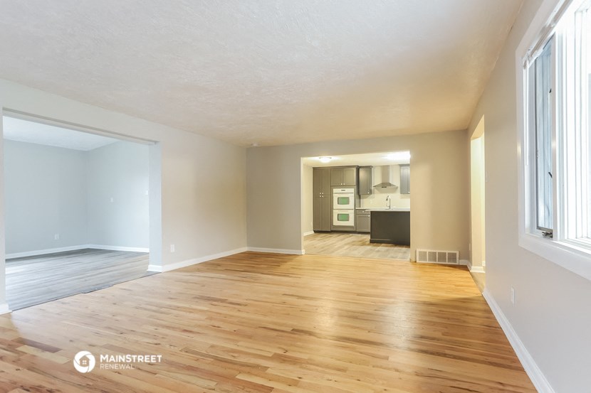 an empty living room with wood floors and a kitchen