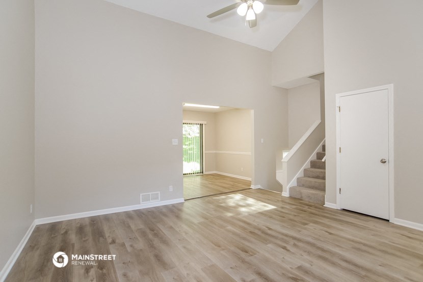the spacious living room with hardwood flooring and a ceiling fan