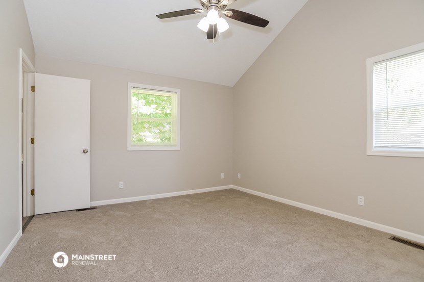 the spacious bedroom with ceiling fan and carpeting