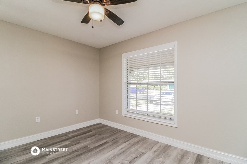 the spacious living room with a large window and a ceiling fan