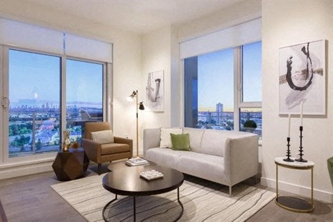 A living room with a white couch, a coffee table, and a large window with a view of the city.