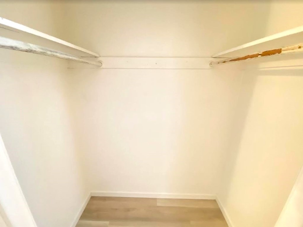 A white closet with a wooden floor and a white shelf.