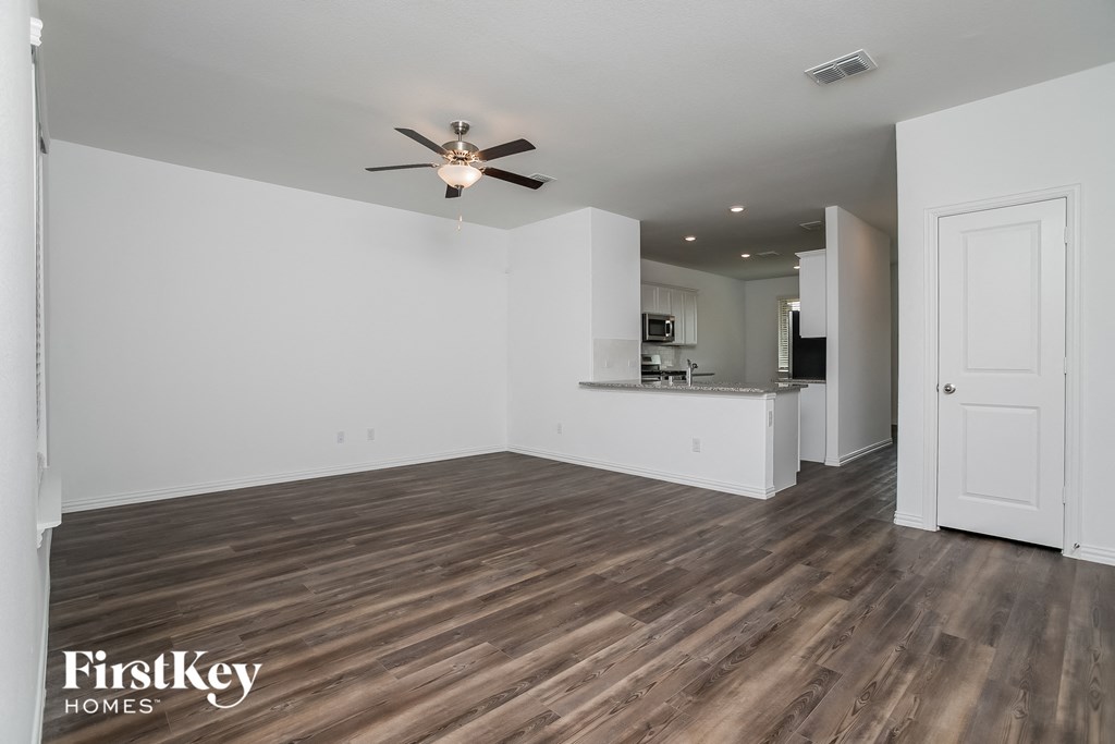 an empty living room with a ceiling fan and a kitchen