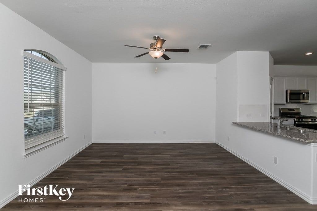 an empty living room with a kitchen and a ceiling fan