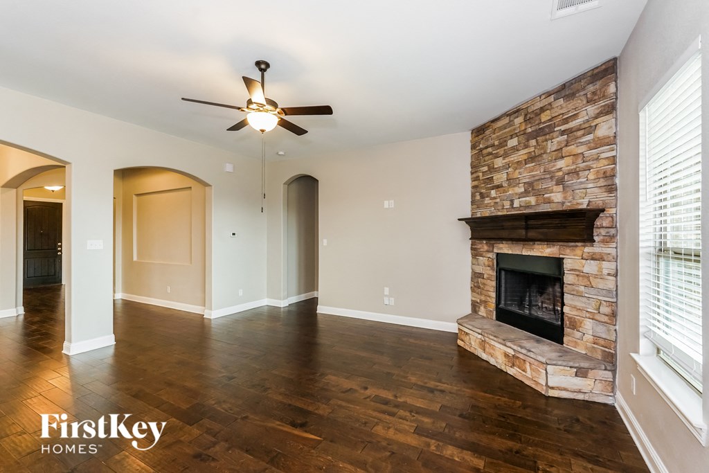 an empty living room with a brick fireplace and a ceiling fan
