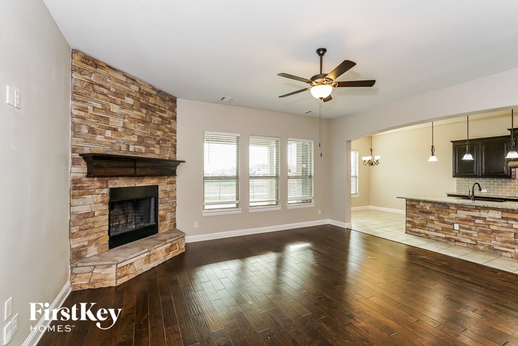 an empty living room with a brick fireplace and a ceiling fan