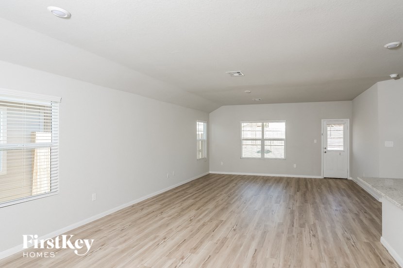A spacious room with wooden flooring and two windows.