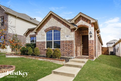 the front of a brick house with a lawn and steps to the front door